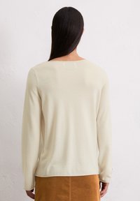 Helle beige Strickpullover mit langen Ärmeln, Rundhalsausschnitt und einer glatten Textur; kombiniert mit einem braunen Wildlederrock.