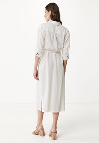 Abito bianco fino al ginocchio con colletto, maniche a tre quarti e cintura. Dettaglio di spacco laterale e bottoni decorativi sulle maniche. Tessuto liscio.