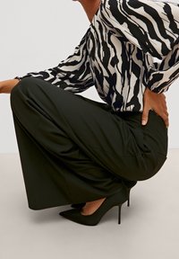 Des chaussures noires à talons aiguilles avec un bout pointu, accompagnées d'une blouse oversized à motifs noirs et blancs et d'un pantalon large noir.