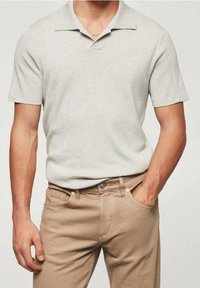 Polo shirt gris clair à manches courtes avec un col texturé, associé à un pantalon beige. Design simple avec une apparence décontractée et subtile.