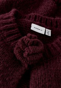 Burgundijas adīts džemperis ar teksturētu ziedu akcentu un ribotām malām. Izsmērētā etiketē rakstīts "name it" ar izmēru 7-8, 122-128. Mīksta, pūkaina sega.