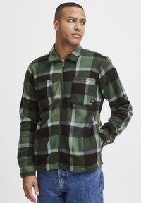 Groene en zwarte geruite fleece jack met rits en kraag, twee borstzakken en een zachte textuur. Bevat grijze accenten in het patroon.