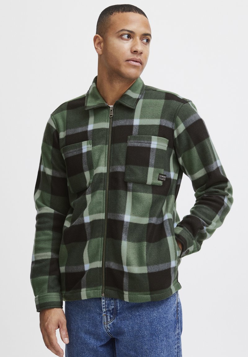 Groene en zwarte geruite fleece jack met rits en kraag, twee borstzakken en een zachte textuur. Bevat grijze accenten in het patroon.