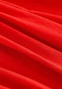 Czerwony materiał o gładkiej, lekko teksturowanej powierzchni, z miękkimi fałdami i zagnieceniami. Kolor jest żywy i jednolity w całej powierzchni.