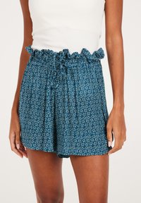 Pantaloni corti blu con un elastico arricciato in vita e cordoncino. Il tessuto ha una consistenza morbida con un motivo floreale ripetuto.