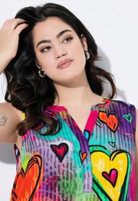 Top senza maniche colorato con una varietà di design a forma di cuore; i materiali appaiono leggeri e non uniformi, con un dettaglio di chiusura a bottone sul collo.