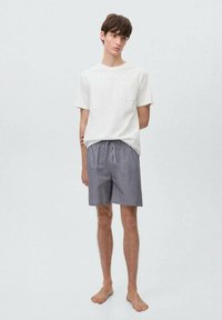 Hvid bomulds T-shirt med lomme, parret med marineblå og hvide stribede shorts. Shortsene har elastisk talje og snørebånd.
