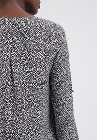 Persoon in een zwart-wit gestreepte langemouwen top, gezien vanuit de achterkant tegen een effen grijze achtergrond.