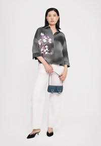 Camicia grigia satinata con motivo floreale rosa, maniche ampie a tre quarti; abbinata a pantaloni bianchi a gamba larga e una piccola borsa in denim.