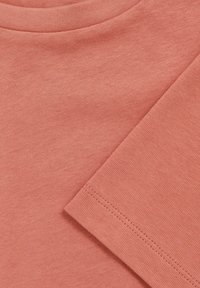 T-shirt i bomuld i en blød koralfarve med rund halsudskæring, der viser en glat tekstur og pæne sting på ærmer og kant.