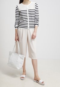 Pruhovaný námořnický a bílý kardigan s krajkovým vsazením, spárovaný s béžovými culottes, bílou taškou a bílými skládacími sandály.