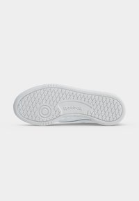 Semelle de chaussure blanche avec un motif en losange et une adhérence circulaire, avec le logo Reebok en relief au centre.