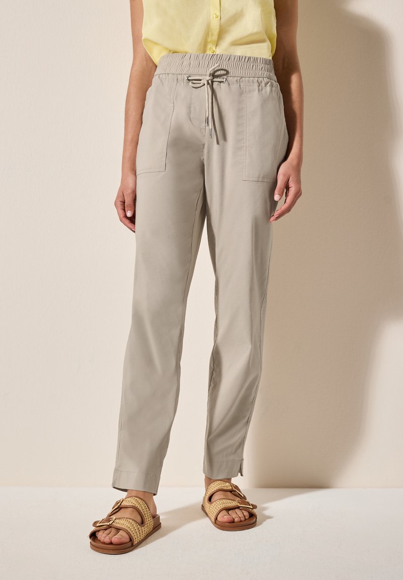 Pantaloni beige leggeri con vita elasticizzata, chiusura con cordoncino e tasche frontali. Abbinati a sandali intrecciati color cammello.