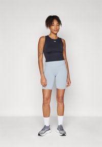 Svart ermeløs topp, lyseblå tettsittende shorts, grå joggesko og hvite sokker. Teksturert stoff med merkevarelogo på toppen.