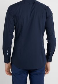 Marineblauw shirt met lange mouwen, rugplooien, afgeronde zoom, manchetknoopjes en contrasterende binnenkant van de manchet. Gladde katoenen stof met een getailleerde pasvorm.