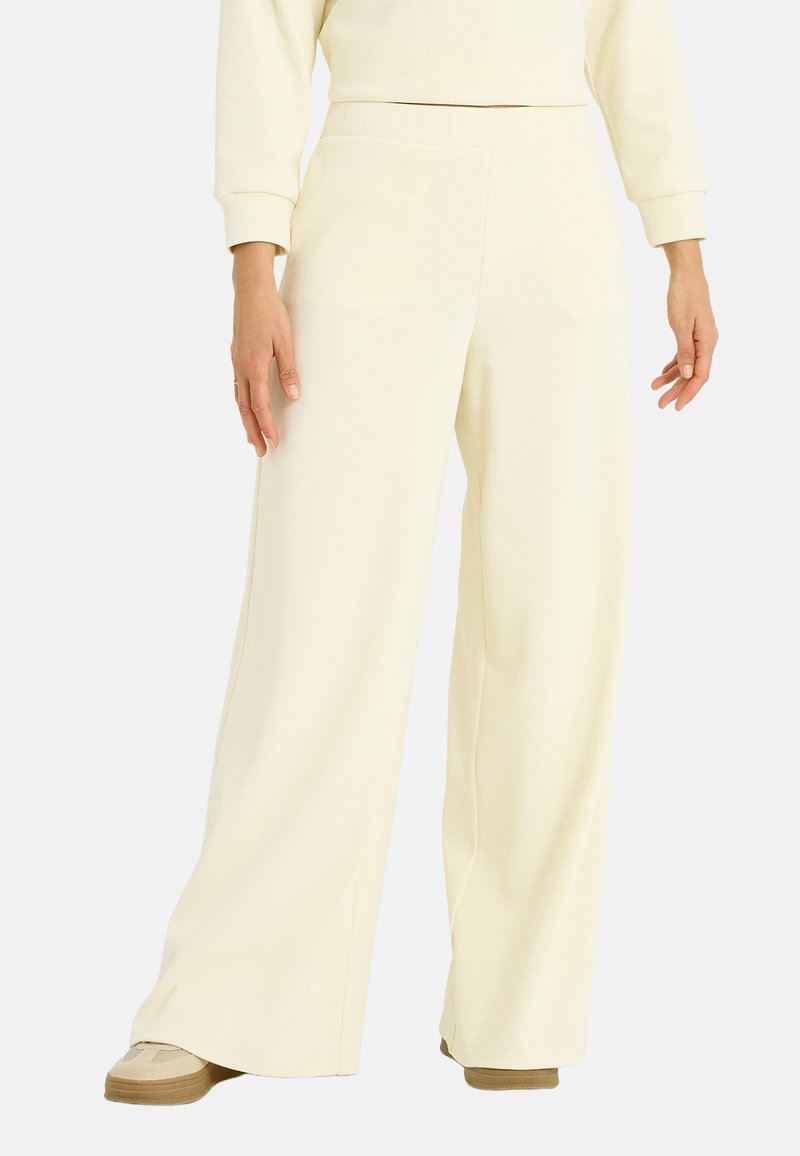 Pantalones de pierna ancha hechos de tela suave y texturizada en un color crema claro. Presentan una cintura alta y un ajuste relajado sin cierres visibles.