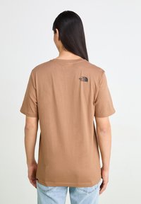 Camiseta de algodón marrón con mangas cortas, escote redondo y detalle del logo en la parte superior de la espalda. Textura suave, corte relajado.