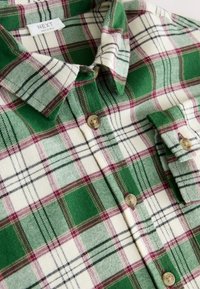 Grün-cremefarbenes kariertes Hemd mit einem Button-Down-Kragen, versehen mit Knöpfen, unterschiedlichen Texturen und einem wollartigen Gefühl.