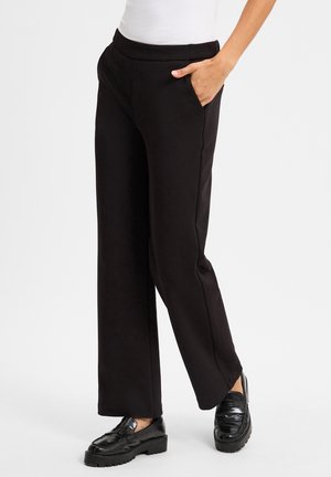 Zwarte wijde pijpen broek van soepel materiaal, met zijzakken en een op maat gemaakte taille. Gecombineerd met glanzende zwarte instappers.