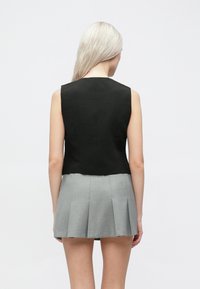 Μαύρη αμάνικη μπλούζα με εφαρμοστή γραμμή, συνδυασμένη με γκρι πλισέ φούστα. Λείο υφασμάτινο υλικό και καθαρές γραμμές. Πίσω όψη.