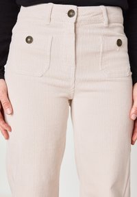 Lichtroze ribfluwelen broek met verticale ribbels, twee voorzakken en metalen knopen bij de taille, met een licht uitlopende pijpdesign.