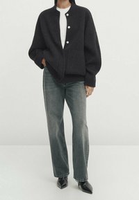 Zwart gebreide cardigan met een ronde kraag, vijf knoopsluiting en oversized mouwen, gecombineerd met slim fit grijze jeans en puntige zwarte hakken.