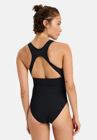 Maillot de bain une pièce noir avec une jambe haute, un design dos nageur et un dos dénudé, fabriqué dans un matériau lisse et extensible.