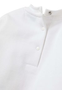 Chemise blanche en coton avec un col haut et une fermeture à bouton pression, une texture lisse et une petite poche à l'avant.
