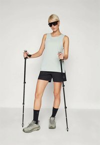 Šviesiai mėlynas beisbolo marškinėlis su apvaliu iškirpimu, derinamas su tamsiais šortais. Asmuo laiko žygių lazdas, dėvi pilkas batus ir tamsius saulės akinius.