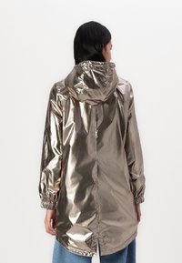 Metalen zilveren regenjas met capuchon, verharde mouwen en een rechte snit. Bevat een reflecterende oppervlakte en een achterkantventilatie voor luchtcirculatie.