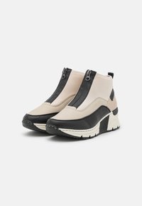 Bottines noires et beige avec une finition texturée, dotées de zips à l'avant, d'une semelle épaisse et d'un design stratifié distinctif.