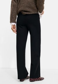 Black wide-leg trousers in a smooth fabric, featuring a simple design. Worn with maroon flats adorned with silver studs.