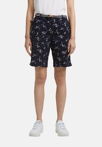 Námořnické šortky s květinovým vzorem, vyrobené z bavlny, s bočními kapsami a tkaným páskem s hnědou přezkou. V kombinaci s bílými teniskami.