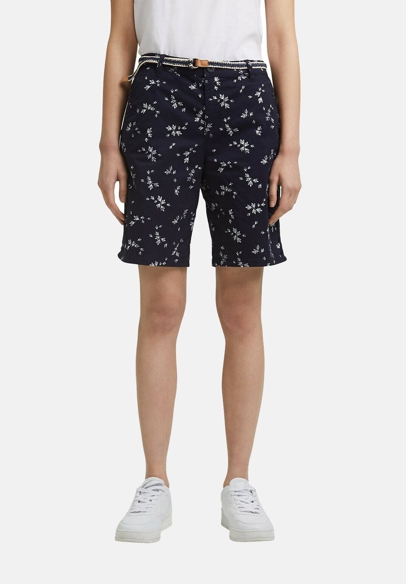 Námořnické šortky s květinovým vzorem, vyrobené z bavlny, s bočními kapsami a tkaným páskem s hnědou přezkou. V kombinaci s bílými teniskami.