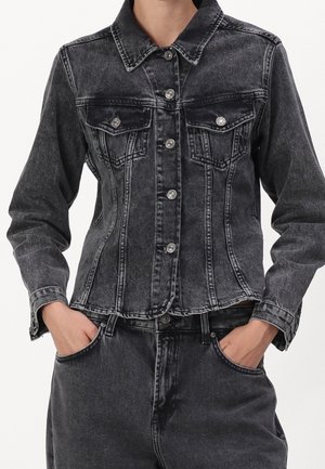 Fadet sort denimjakke med sølvknapper båret over matchende højttaljede jeans, hænderne i lommerne, forfra, ansigt ikke synligt.