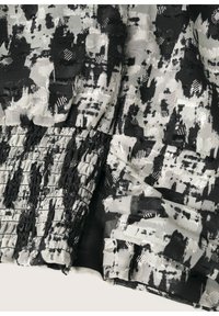 Sort og hvidt mønstret stof med teksturerede smock-detaljer, der har en blanding af glatte og ru overflader. Dekorativ stitching er synlig.