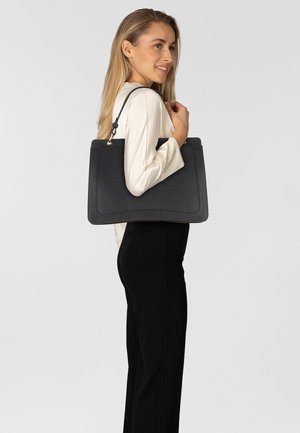 Borsa tote nera con texture e forma strutturata, dotata di due manici e di un dettaglio liscio sulla parte anteriore. Portata da una modella.