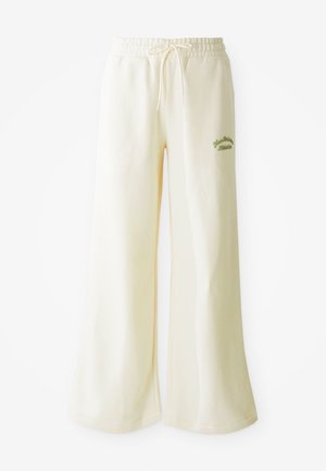 Pantalons de survêtement larges crème avec une taille élastique et un cordon de serrage ajustable. Texte "Athletic" brodé en vert à l'avant. Tissu doux.