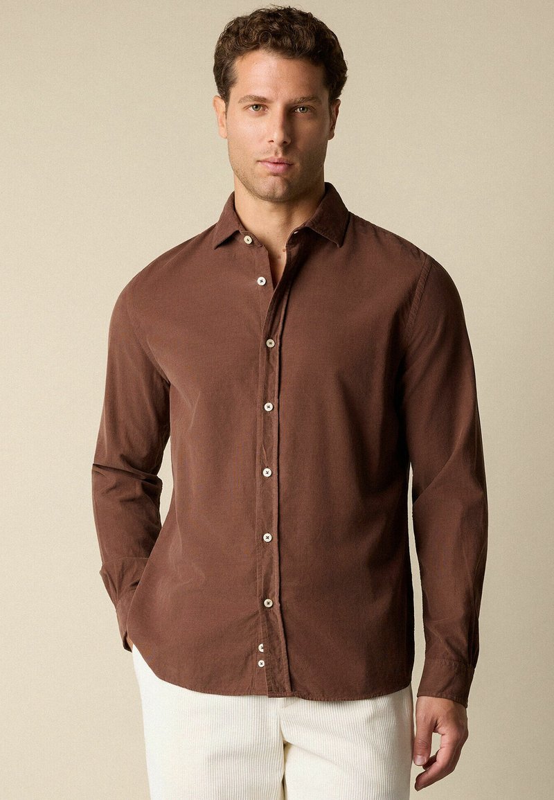 Bruine button-up shirt van lichtgewicht stof met een kraag, lange mouwen en witte knopen. Gedragen met textuurovergoten crèmekleurige broek.