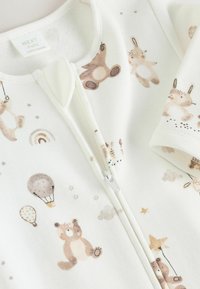 Combinaison en polaire blanche pour bébé avec un zip à l'avant, ornée d'illustrations douces d'animaux, de montgolfières et d'étoiles dans des teintes beige et pastel.