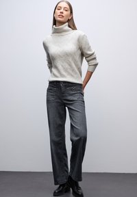 Suéter de punto gris claro con cuello alto y patrón texturizado, combinado con vaqueros de mezclilla gris oscuro de corte relajado y botas negras hasta el tobillo.
