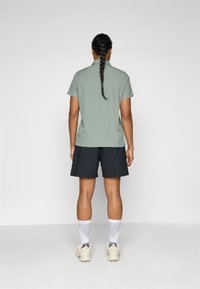 Kortærmet lysegrøn skjorte, sorte shorts, hvide sokker og beige sko. Håret sat i en fletning. Simpelt, funktionelt design.