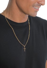 Auksinės spalvos grandinėlės vėrinys su kryžiaus pakabuku, lygios tekstūros ir sujungtų grandelių dizainu, dėvimas ant juodos spalvos marškinėlių.