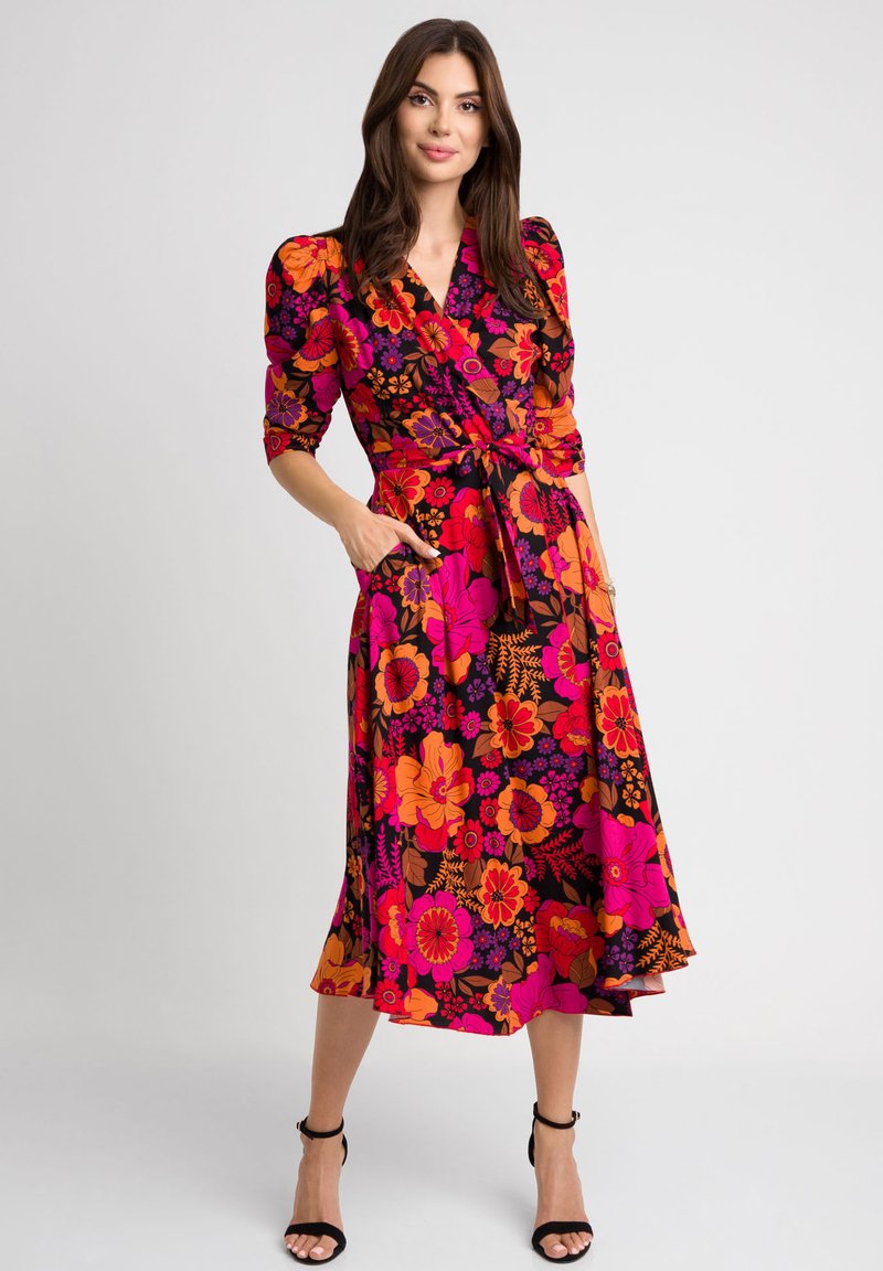 Kwiatowa sukienka w stylu wrap, wyróżniająca się intensywnymi kolorami różu, pomarańczu i czerni, z rękawami 3/4, paskiem w talii oraz kieszeniami po bokach.