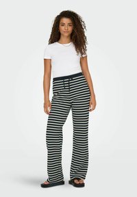 Striped wide-leg pants in navy and cream, with a drawstring waist and soft fabric. Paired with a plain white t-shirt and black sandals.