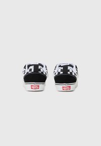 Svartvita rutiga slip-on skor med mocka-häl och vit sula. Har Vans-logotyp på hälen och tådetaljer.
