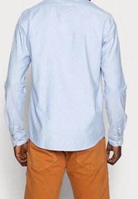 Lichtblauw, lang mouw shirt met een button-down kraag en manchetten, gecombineerd met oranje broek met achterzakken en een gestructureerde stof.