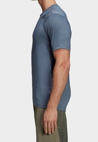 Jasnoniebieska koszulka sportowa z krótkim rękawem, wykonana z teksturowanej, przewiewnej tkaniny. Wyróżnia się okrągłym dekoltem i subtelnym logotypem na ramieniu.