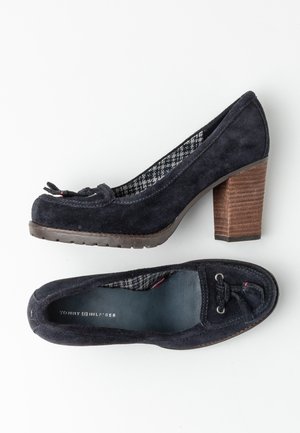 Mocasines de tacón para mujer en ante navy con detalle de moño trenzado y tacón de bloque de madera apilada, forro interior de pata de gallo y marca Tommy Hilfiger.