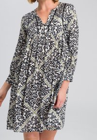 Robe en imprimé léopard avec des manches longues, décolleté en V et buste plissé. Présente un motif géométrique vert contrastant et un tissu léger.